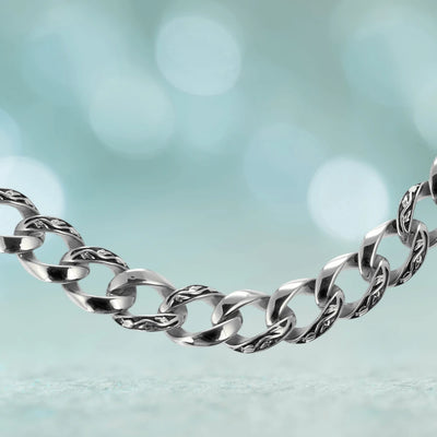 Close-up of a male stainless steel Enigma Steel Necklace featuring polished and textured interlocking links against a soft blue blurred background.