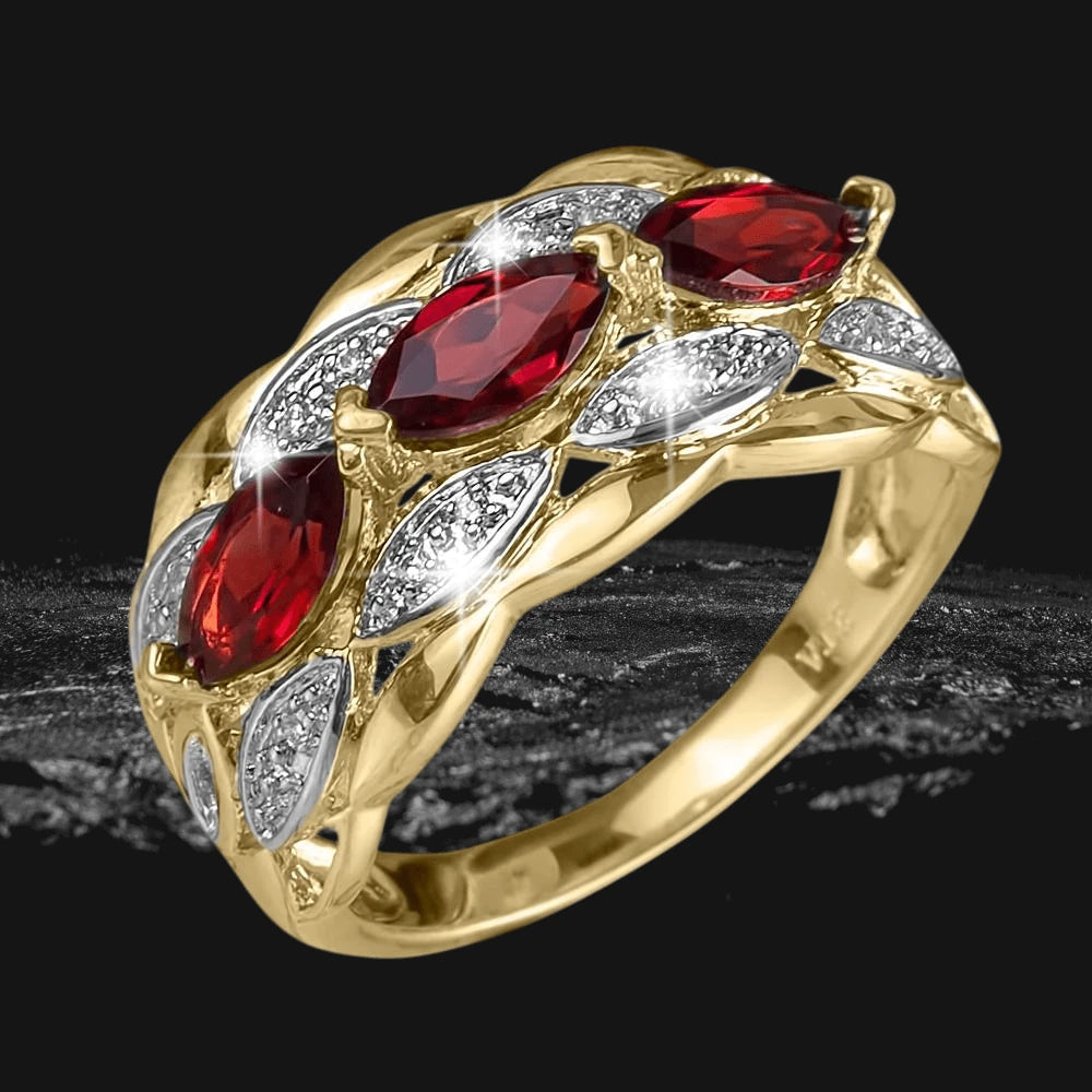 Garbo Garnet Ring featuring a sterling silver base plated in gold with three marquise-cut red garnet stones and diamond-accented details, designed for women’s jewelry collection.