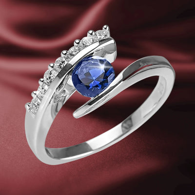 Eva Blue Ring featuring a sterling silver band with rhodium plating, adorned with a striking blue gemstone and accented by sparkling clear stones, designed for women’s jewelry.