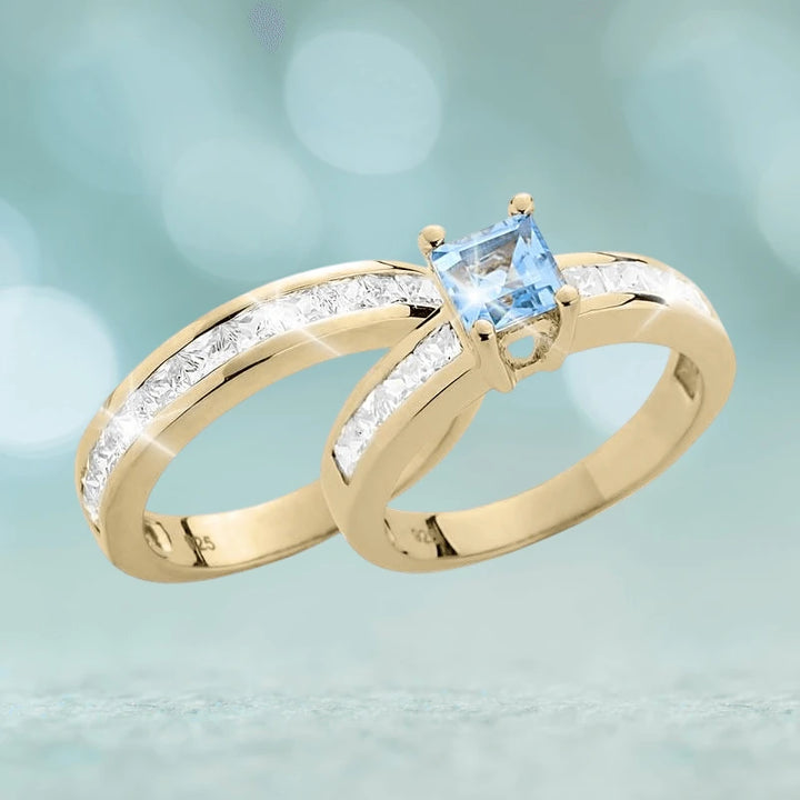 Maria Duo Blue Topaz Bridal Ring set in sterling silver with gold plating, featuring a square blue topaz center stone and channel-set clear stones on the bands.