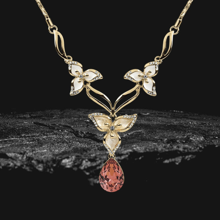 Calla Flora Necklace in gold plating featuring an elegant floral design with white enamel accents and a teardrop-shaped pink gemstone pendant.
