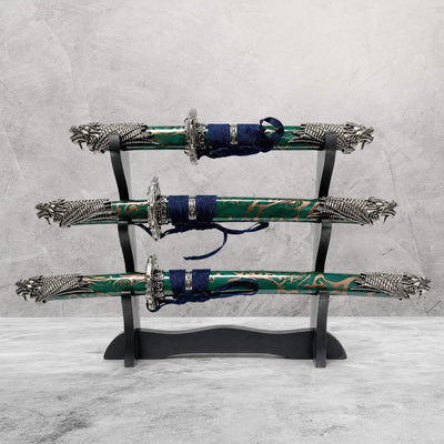 Jade Dragon Sword Set displayed on a black wooden stand featuring three intricately designed swords with green and gold patterned sheaths and detailed silver dragon-themed handles, Up To 75% Off Retail.