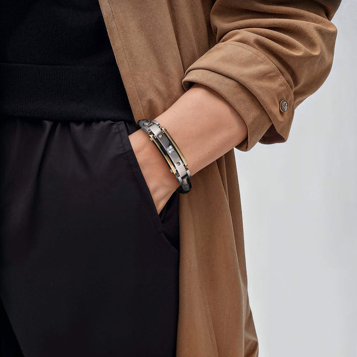 Close-up of a person wearing the Men's Diamond Leather Bracelet featuring steel and leather materials with a two-tone plating color, styled with a brown coat and black pants.