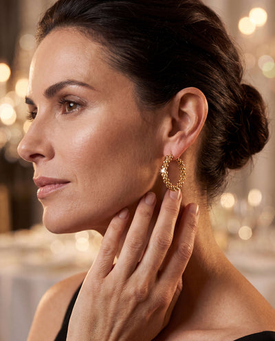 Close-up of a woman wearing Roma Luxe Beaded Earrings in gold-plated bronze, showcasing elegant jewelry with a warm, soft background, Up To 75% Off Retail.