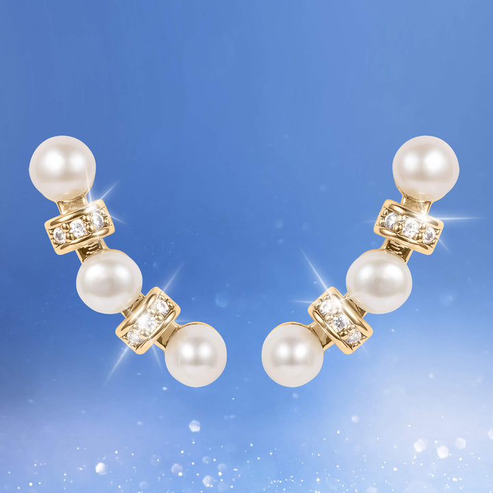 Aria Pearl Earrings featuring three lustrous pearls connected by gold-tone links accented with sparkling crystals, captured against a soft blue sparkling background with Up To 75% Off Retail.