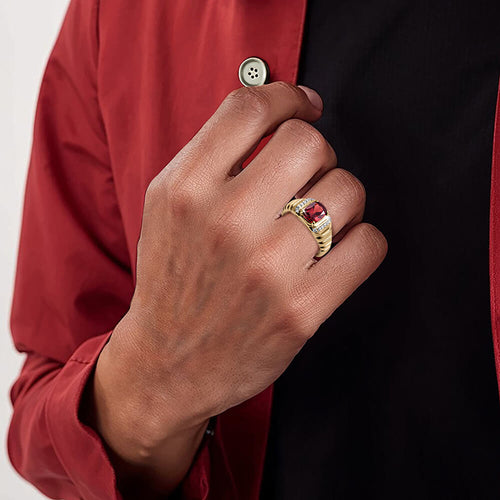 Hand wearing a gold ring with a red stone on a red shirt background