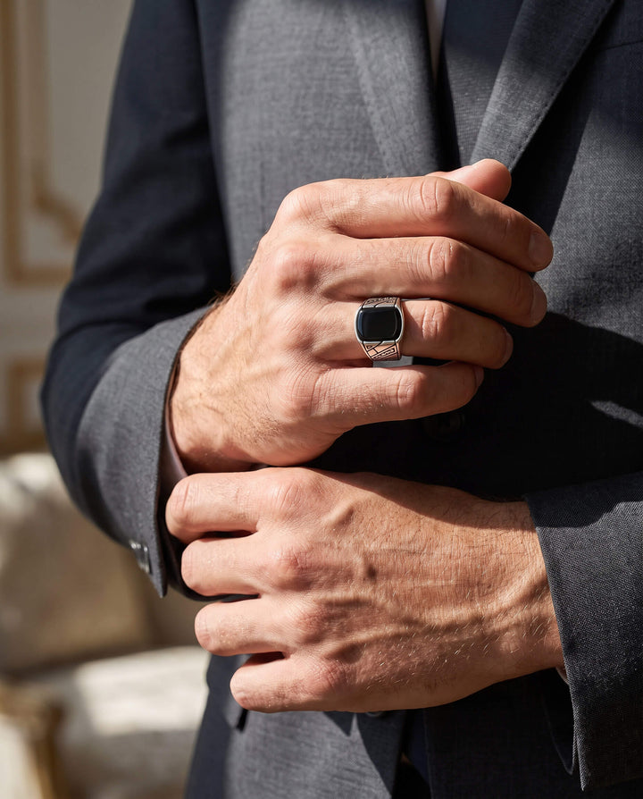Man dressed in a sharp suit wearing the Onyx Raven Men's Ring with a black stone and detailed silver band, showcasing elegance and style, Up To 75% Off Retail.