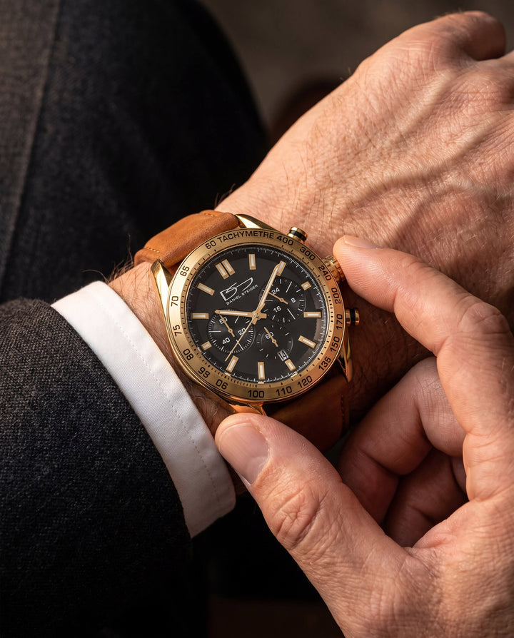 A close-up of a person adjusting the gold-tone Citadel Chrono Men's Watch with a black dial and brown leather strap, showcasing its elegant design and chronograph features, Up To 75% Off Retail.