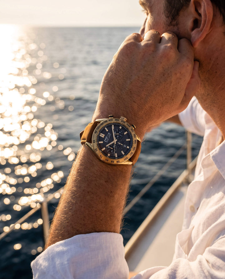 Man wearing a Citadel Chrono Men's Watch with a tan leather strap, gazing over sunlit ocean waters on a boat, promoting up to 75% off retail.