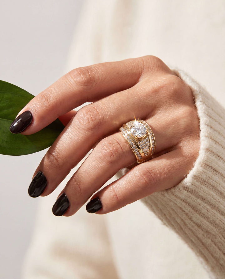 Nova Glow Ladies Ring in gold plating on a female hand with dark polished nails, showcasing a sparkling central gemstone and detailed craftsmanship, Up To 75% Off Retail.
