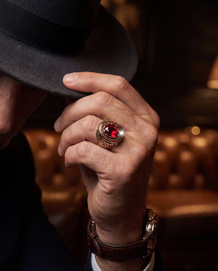 Royal Inferno Men's Ring in gold-plated stainless steel featuring a large red gemstone, worn on a man's hand adjusting a black fedora, Up To 75% Off Retail.