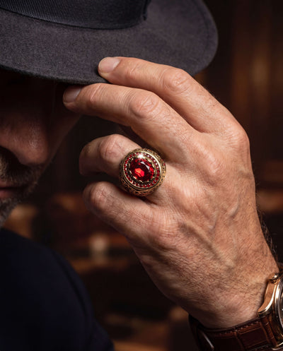 Close-up of a male hand wearing the Royal Inferno Men's Ring made of gold-plated stainless steel with a large red stone, highlighting luxury jewelry design, Up To 75% Off Retail.