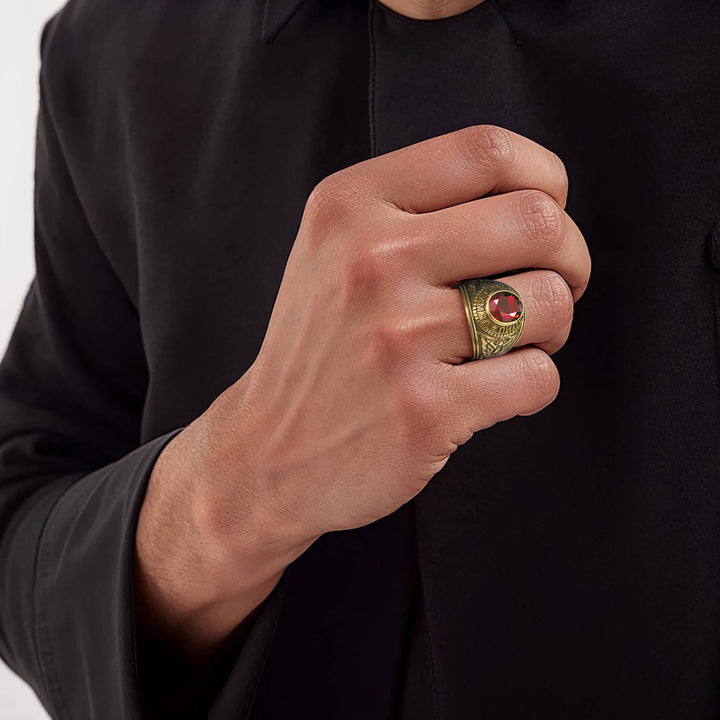 Male hand wearing a gold-plated stainless steel Army Ring with a red gemstone, highlighted against a black long-sleeve shirt, showcasing bold jewelry style.