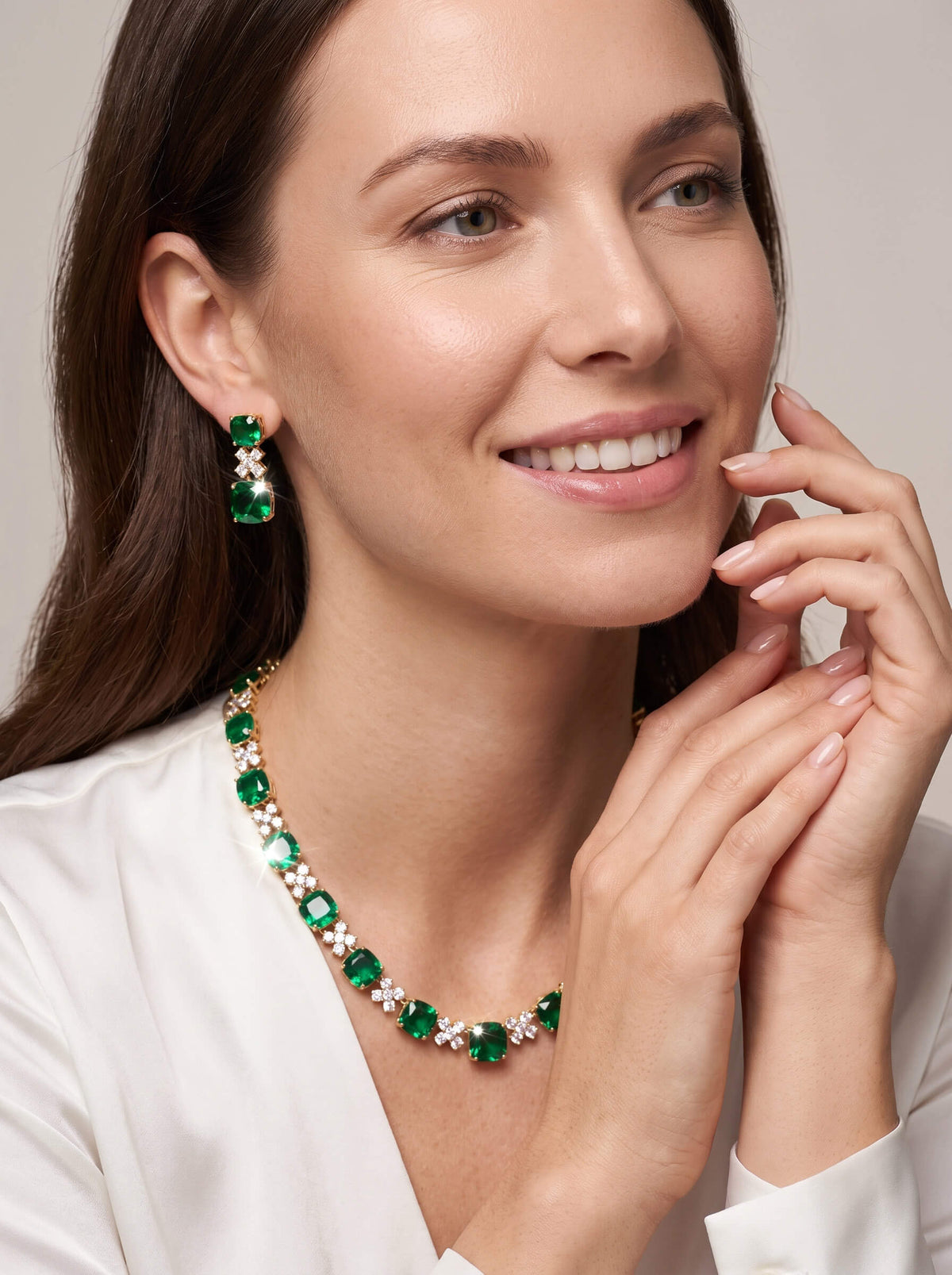 Woman wearing Freya Earrings with sparkling green drop stones and a coordinated necklace, styled with an elegant white blouse. Up To 75% Off Retail