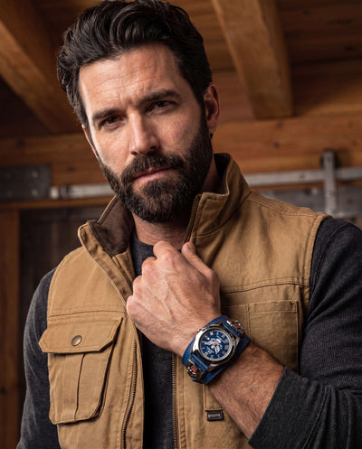Man wearing a brown vest and black shirt showcasing the Patriot 250 Years Blue Limited Edition Watch with a blue dial and stainless steel case, Up To 75% Off Retail.