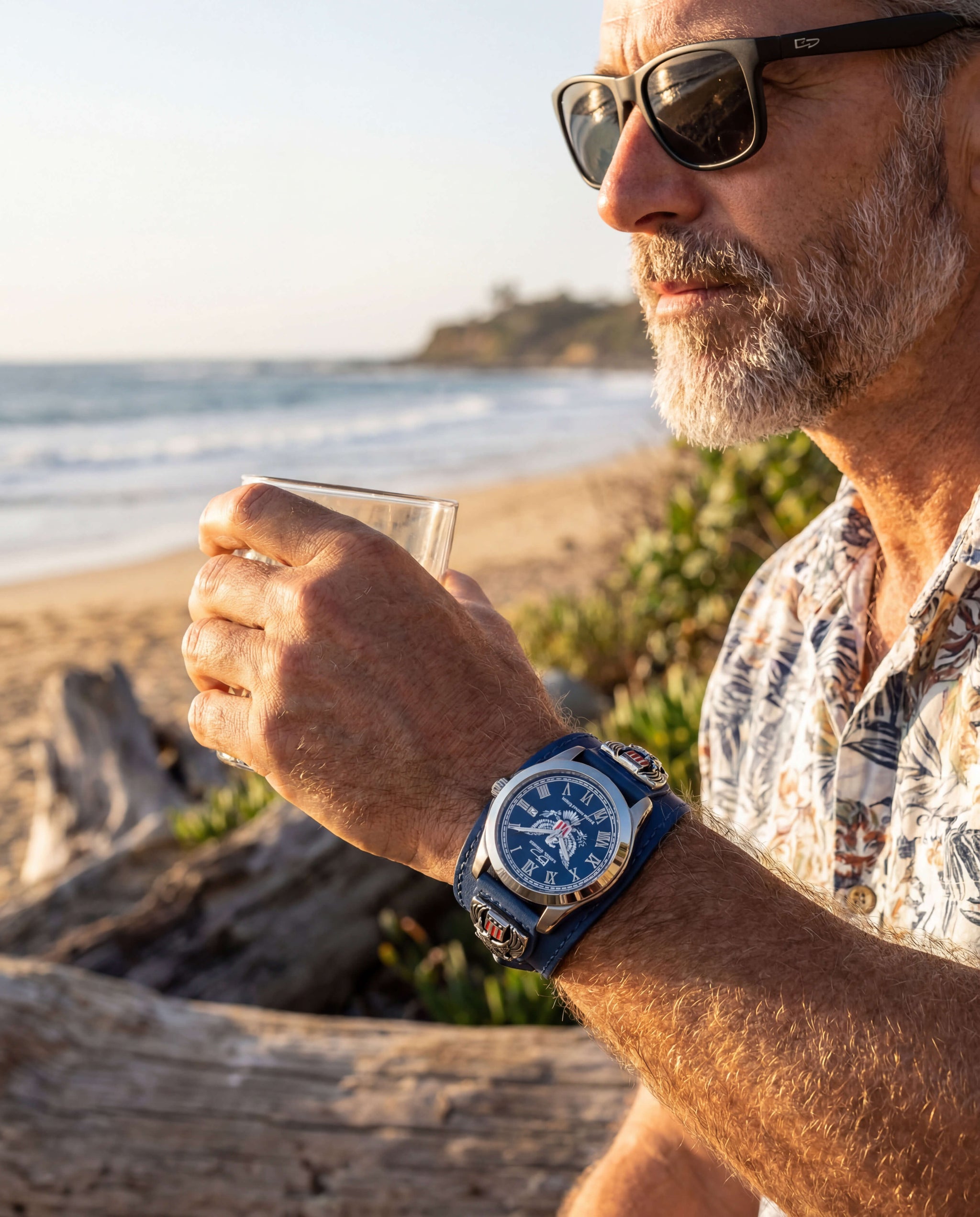 Man wearing sunglasses and a floral shirt at the beach, showcasing the Patriot 250 Years Blue Limited Edition Watch with a stainless steel case and blue dial, enjoying a drink. Up To 75% Off Retail.