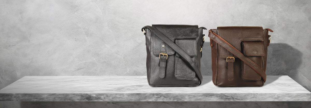 Two leather crossbody messenger bags in black and brown displayed on a white marble shelf against a textured gray background